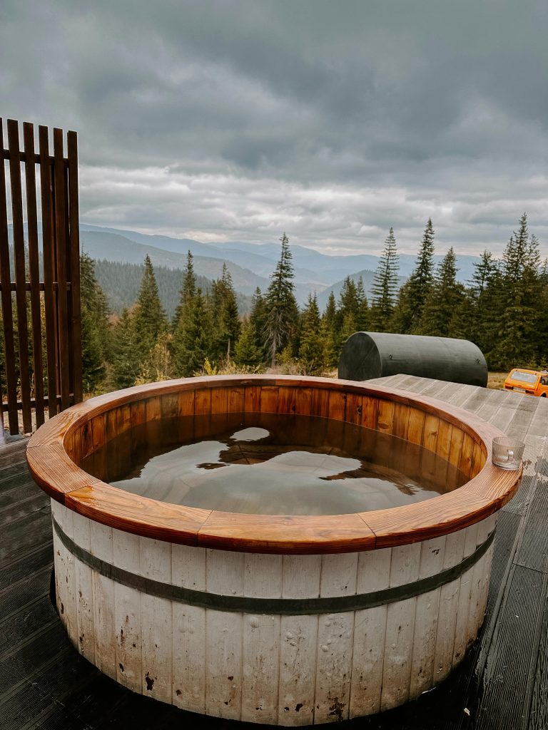 Rustic wooden hot tub on a deck with scenic mountain forest view.