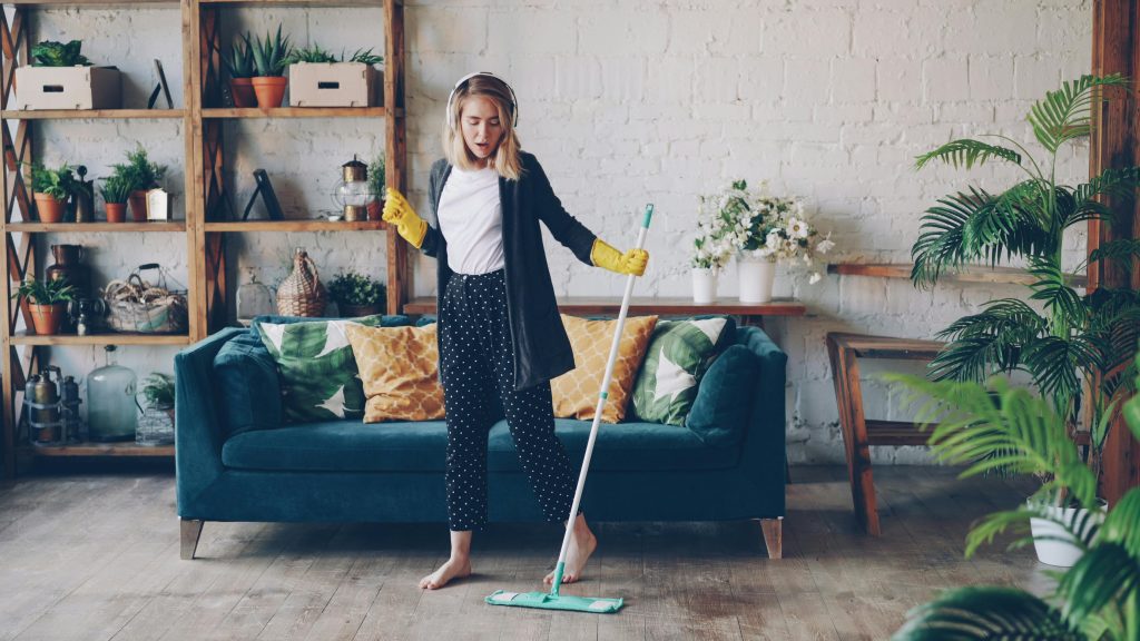 Woman cleaning living room with a mop at home, enjoying music.