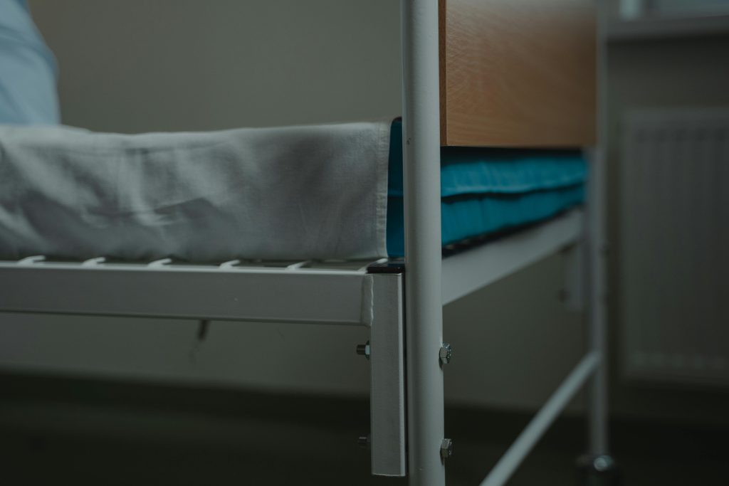Close-up view of a hospital bed with white linens and metal frame, indoors.