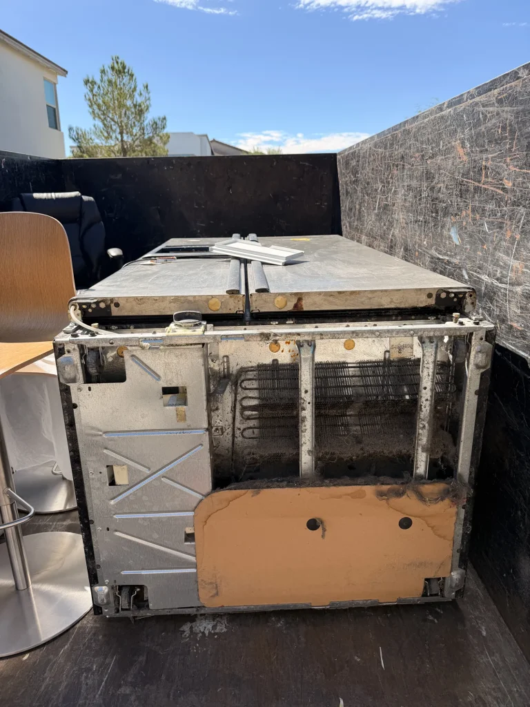 Stainless French-door refrigerator loaded intact in a junk removal trailer for recycling